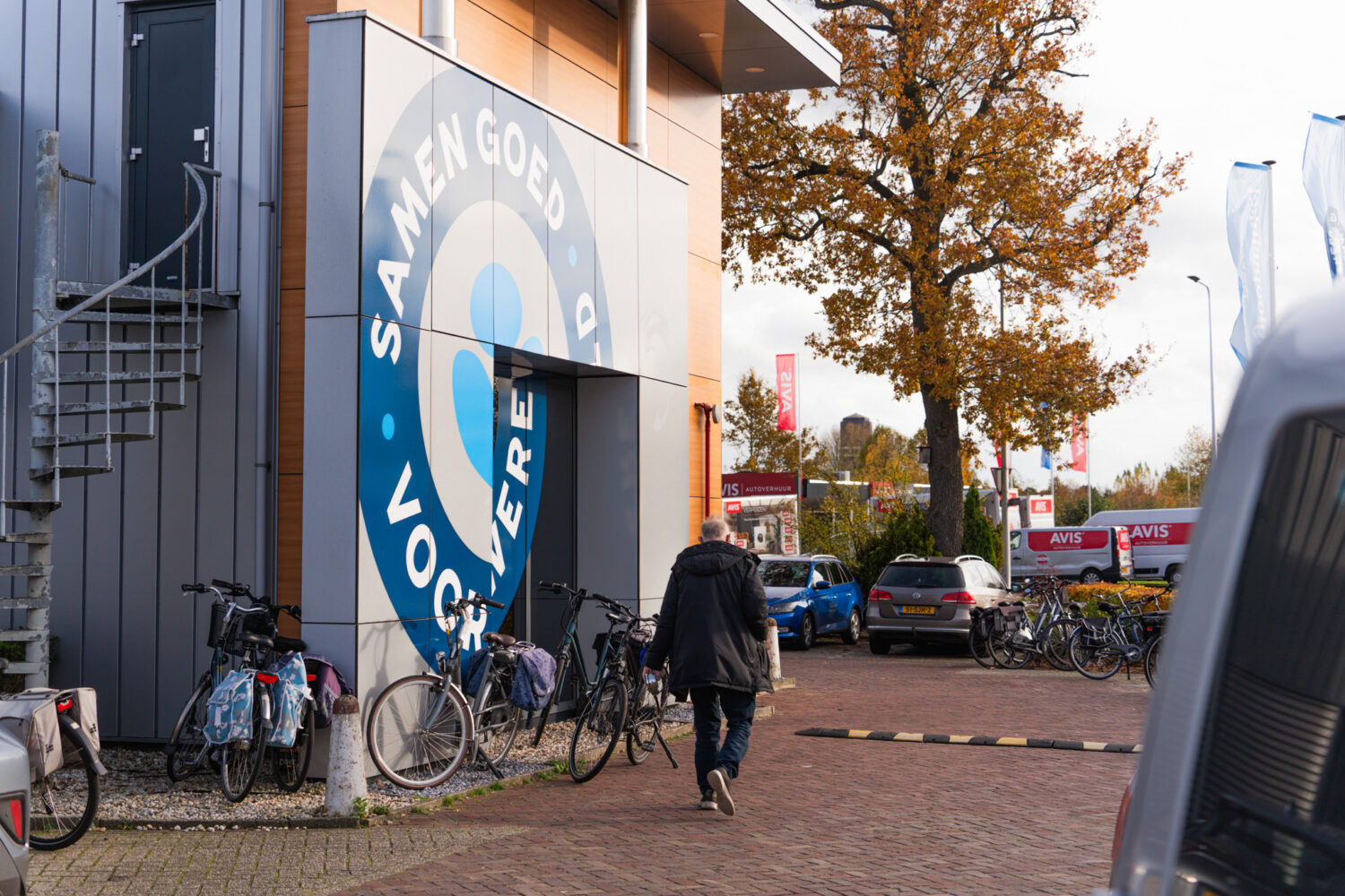 Vrijwilliger in actie bij Dorcas, betrokken bij het ondersteunen van lokale gemeenschappen en het werk voor een eerlijke wereld, met fietsen en kleurrijke herfstbomen op de achtergrond.