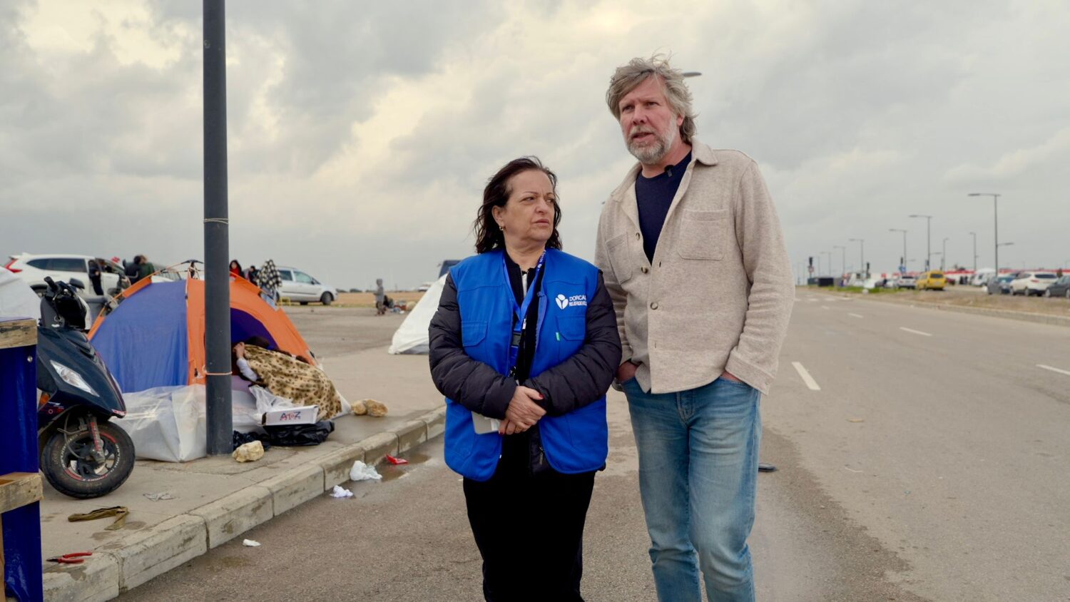 Een hulpverlener en een vrijwilliger staan samen op een parkeerplaats in Libanon, waar vluchtelingen worden geholpen door EO Metterdaad in de context van de noodhulpactie.