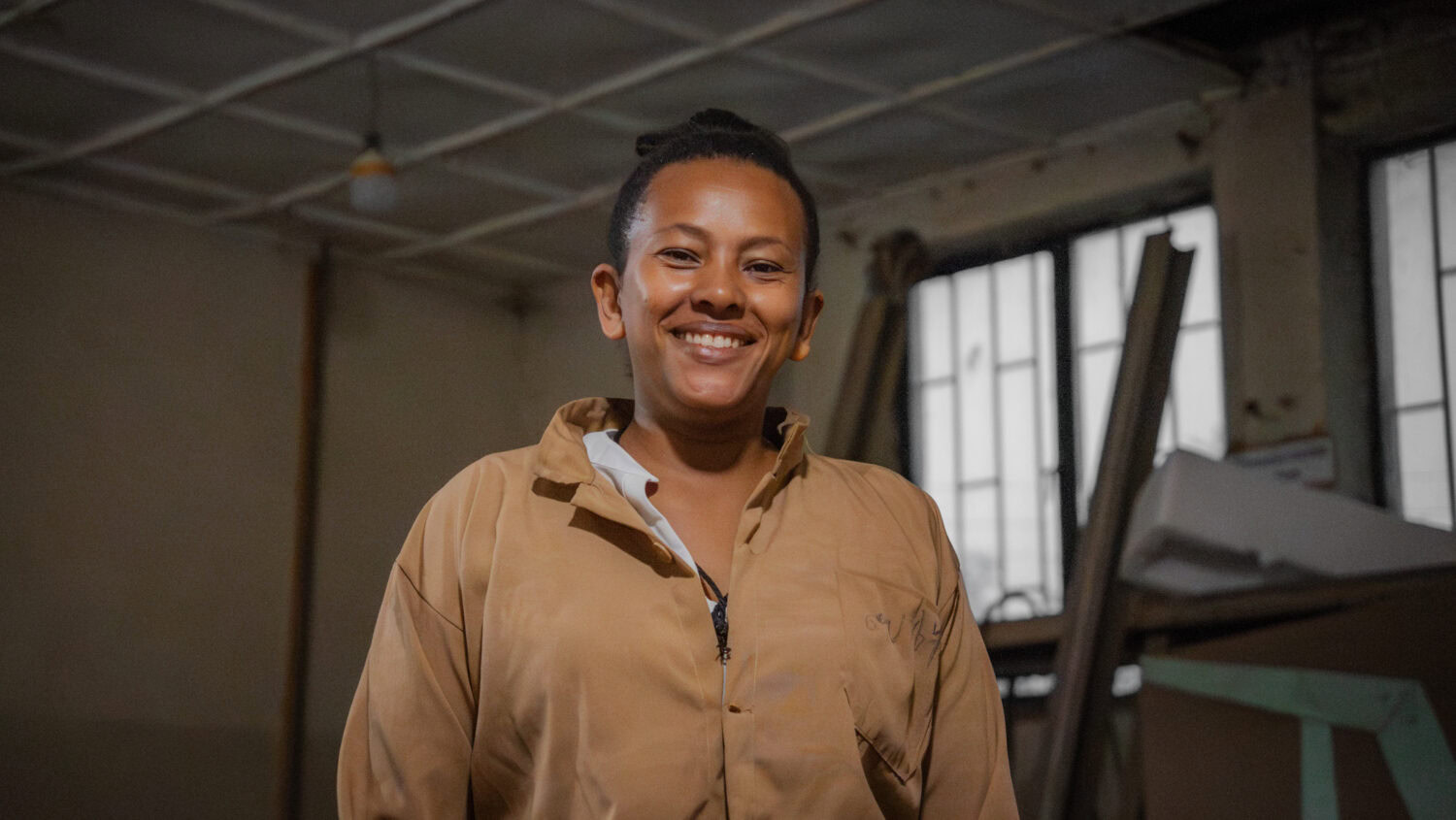 Vrolijke vrouw in een industrieel atelier die werkt aan nieuwe ideeën en concepten voor duurzame projecten, passend bij de thema's van Dorcas en automatische conceptontwikkeling.
