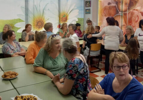 Gezellig bijeenkomst met mensen die in gesprek zijn, in een kleurrijke ruimte met muurdecoraties van bloemen en lachende kinderen, georganiseerd door Dorcas.